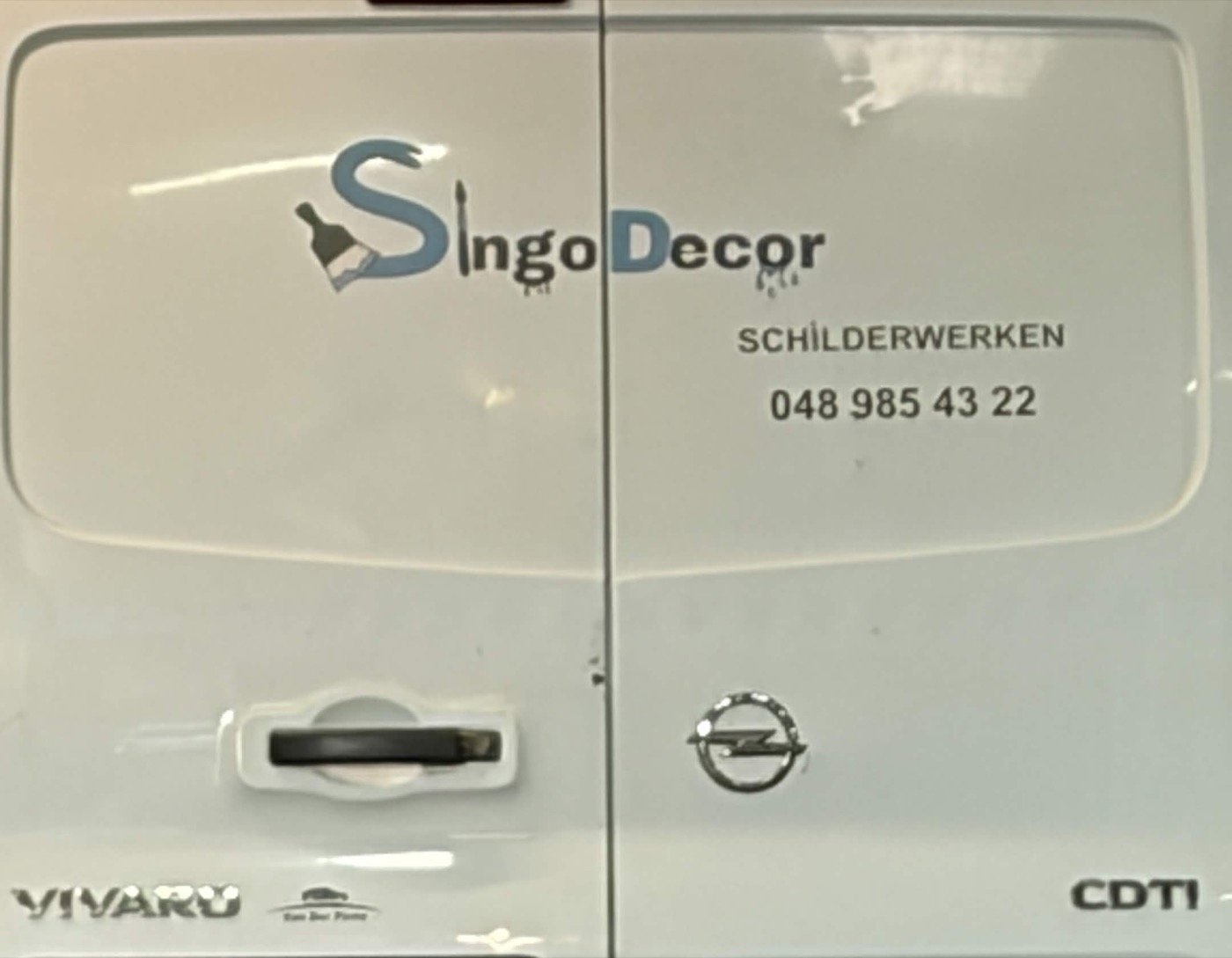 Achterzijde van de witte bestelwagen van Singo Decor met logo, de tekst Schilderwerken en het telefoonnummer 0489 85 43 22.